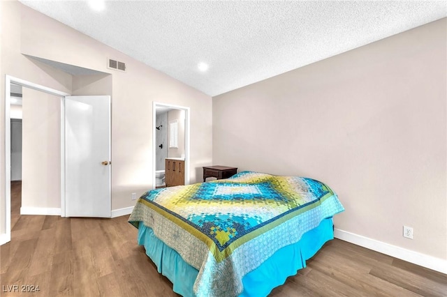 bedroom featuring hardwood / wood-style flooring, a textured ceiling, connected bathroom, and vaulted ceiling