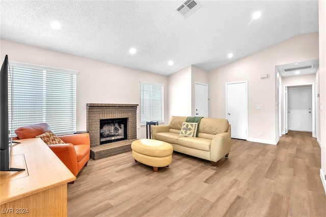 living room featuring a brick fireplace, a textured ceiling, light hardwood / wood-style floors, and vaulted ceiling