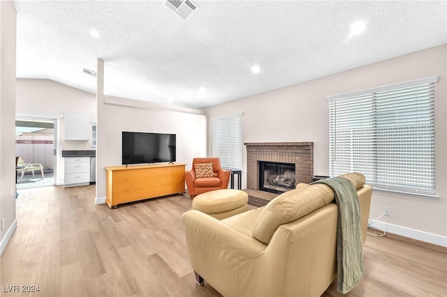 living room with a fireplace, light wood-type flooring, vaulted ceiling, and a wealth of natural light