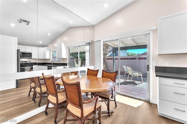 dining room featuring light hardwood / wood-style floors, sink, a textured ceiling, and high vaulted ceiling