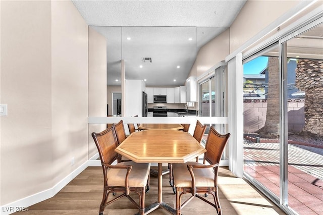 dining room with a textured ceiling, sink, wood-type flooring, and vaulted ceiling