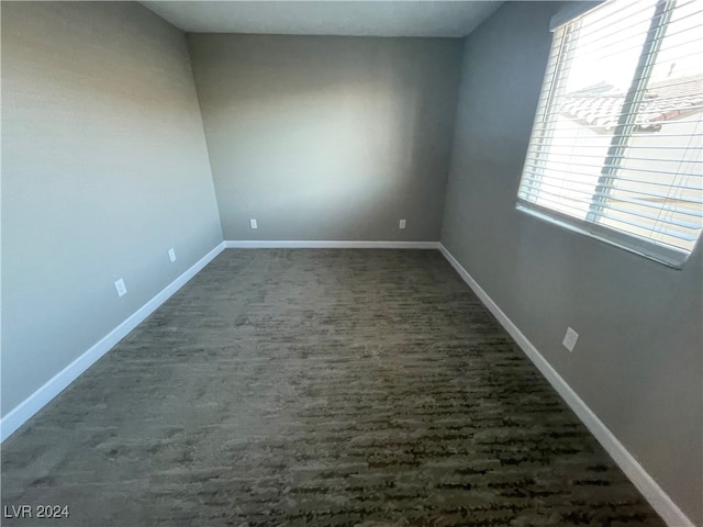 spare room featuring dark colored carpet and a wealth of natural light