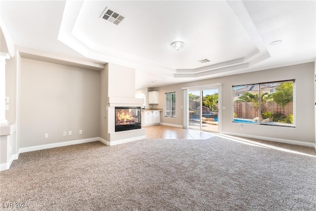 unfurnished living room featuring light carpet, a tray ceiling, and a multi sided fireplace