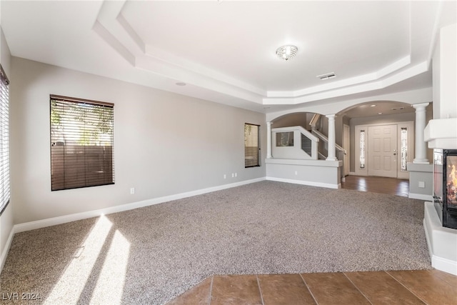 unfurnished living room with decorative columns, carpet flooring, and a tray ceiling