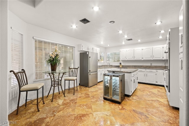 kitchen with appliances with stainless steel finishes, wine cooler, a kitchen breakfast bar, a center island, and white cabinetry