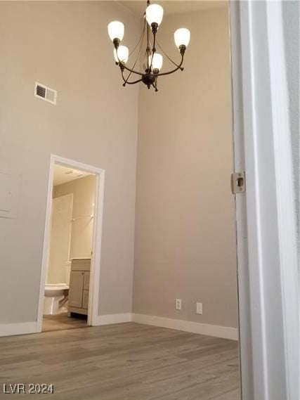 unfurnished room with hardwood / wood-style floors, a towering ceiling, and a notable chandelier