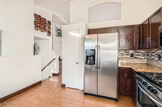 kitchen with light stone countertops, stainless steel appliances, backsplash, dark brown cabinets, and light wood-type flooring