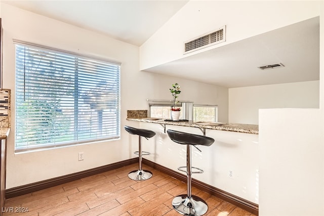 kitchen featuring light wood-type flooring, stone counters, and vaulted ceiling