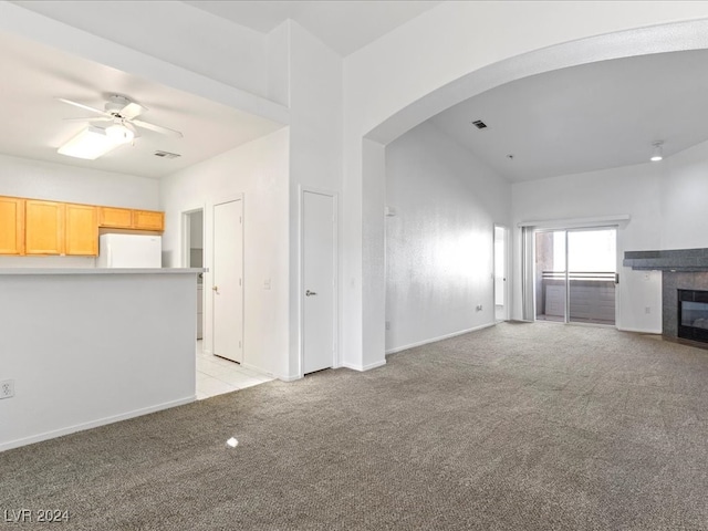 unfurnished living room with a tile fireplace, light carpet, and ceiling fan