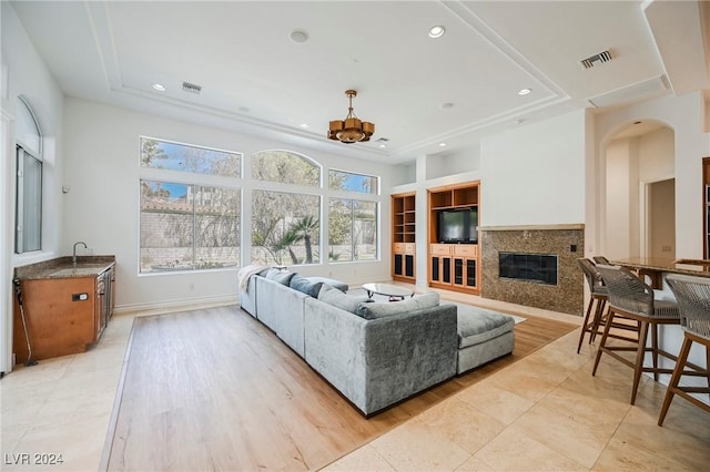 living room with sink, light hardwood / wood-style flooring, a premium fireplace, a tray ceiling, and built in shelves