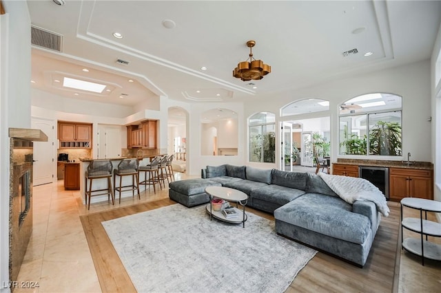 living room with sink, wine cooler, light hardwood / wood-style floors, and a tray ceiling