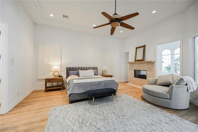 bedroom with a tiled fireplace, wood-type flooring, and ceiling fan