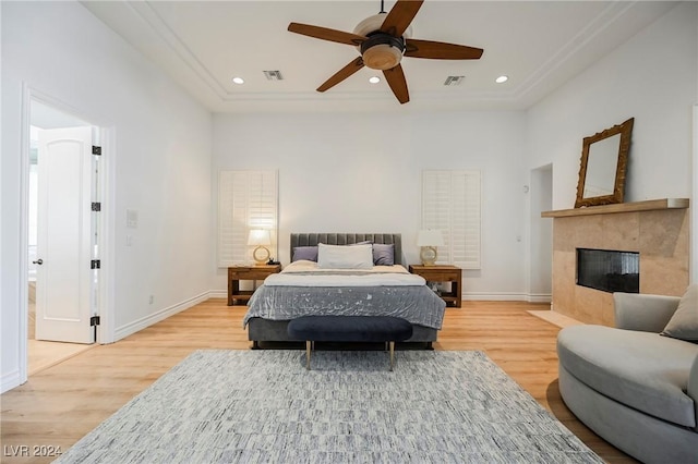 bedroom with a tile fireplace, light wood-type flooring, and ceiling fan