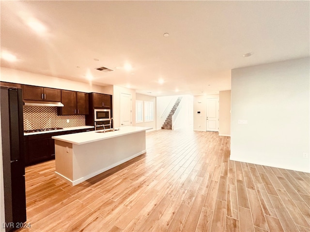 kitchen featuring dark brown cabinetry, a kitchen island with sink, sink, light hardwood / wood-style floors, and stainless steel microwave