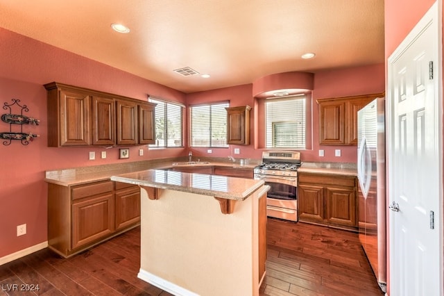 kitchen featuring a center island, sink, dark hardwood / wood-style floors, appliances with stainless steel finishes, and a kitchen bar