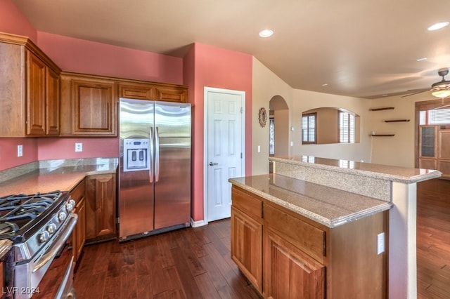 kitchen with ceiling fan, dark hardwood / wood-style floors, a kitchen island, light stone counters, and stainless steel appliances