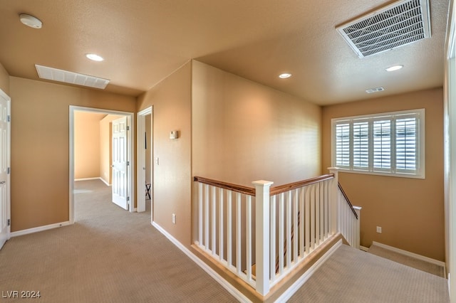 hall with light colored carpet and a textured ceiling