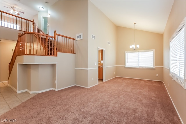 unfurnished living room featuring ceiling fan with notable chandelier, light colored carpet, and high vaulted ceiling