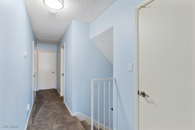 hallway featuring dark carpet and a textured ceiling