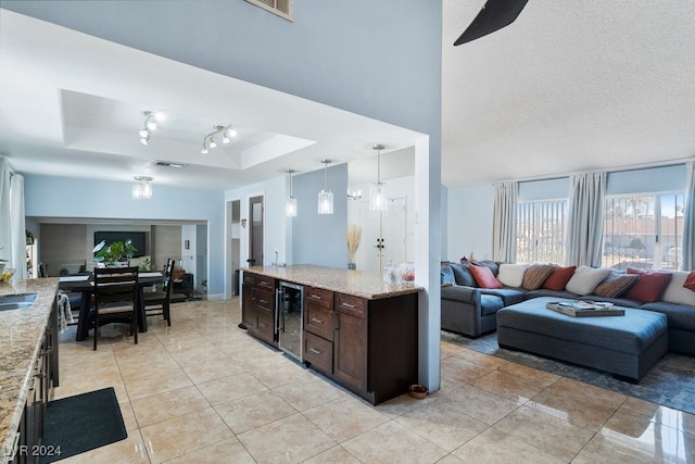 kitchen featuring a raised ceiling, hanging light fixtures, wine cooler, light stone counters, and dark brown cabinetry