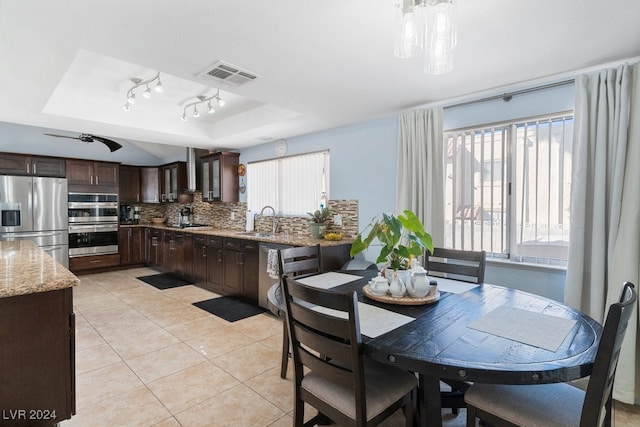 kitchen with light stone counters, dark brown cabinetry, stainless steel appliances, a tray ceiling, and sink