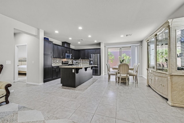 kitchen featuring a kitchen bar, decorative backsplash, a center island with sink, light tile patterned flooring, and appliances with stainless steel finishes