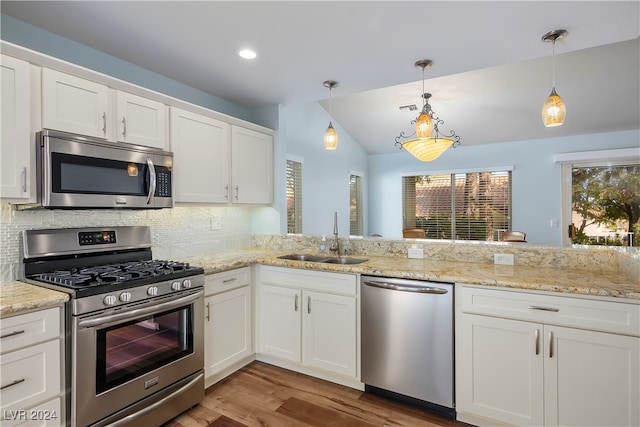 kitchen with kitchen peninsula, appliances with stainless steel finishes, vaulted ceiling, sink, and hanging light fixtures