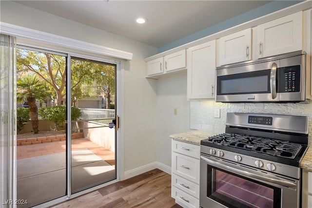 kitchen featuring backsplash, white cabinets, light stone countertops, appliances with stainless steel finishes, and light hardwood / wood-style floors