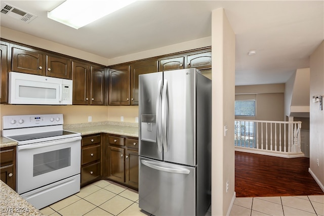 kitchen with white appliances, light hardwood / wood-style flooring, dark brown cabinetry, and light stone counters