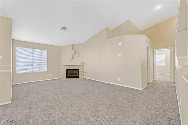 unfurnished living room with light carpet, high vaulted ceiling, and a tiled fireplace