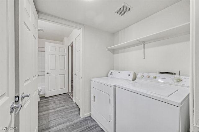 clothes washing area with washer and clothes dryer and light wood-type flooring