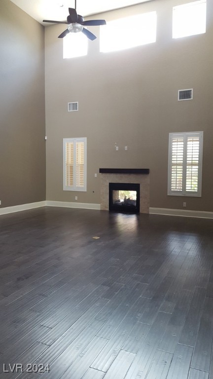 unfurnished living room with ceiling fan, a towering ceiling, and dark wood-type flooring