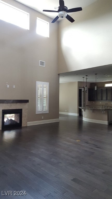 unfurnished living room featuring ceiling fan, dark hardwood / wood-style flooring, and a high ceiling