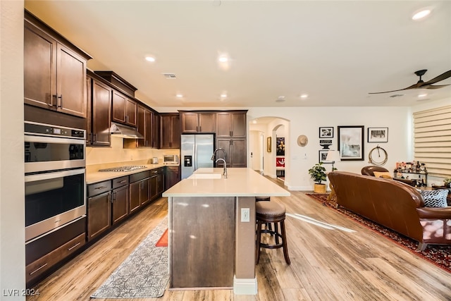 kitchen featuring dark brown cabinetry, an island with sink, a breakfast bar, appliances with stainless steel finishes, and light wood-type flooring