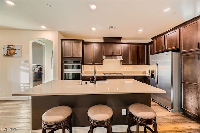 kitchen with an island with sink, stainless steel appliances, and light wood-type flooring