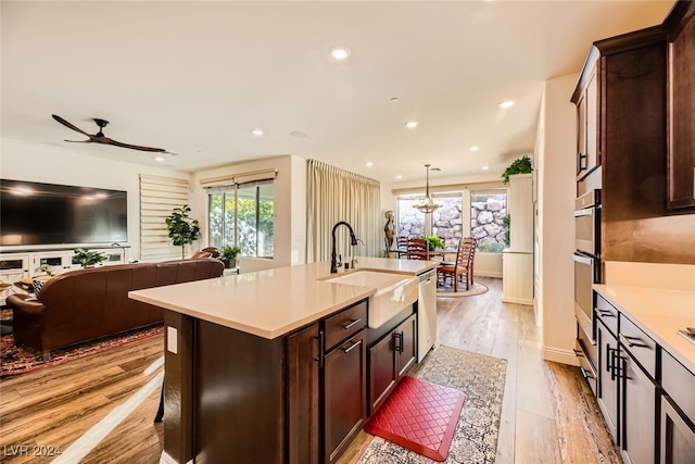 kitchen with sink, decorative light fixtures, dishwasher, light hardwood / wood-style floors, and an island with sink