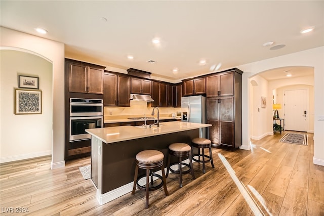 kitchen with a center island with sink, a breakfast bar, appliances with stainless steel finishes, and light hardwood / wood-style flooring