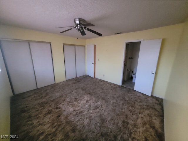 unfurnished bedroom featuring ceiling fan, dark colored carpet, ensuite bathroom, a textured ceiling, and two closets