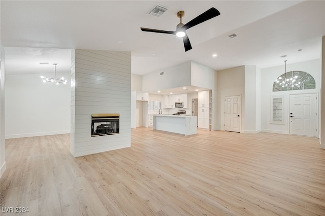 unfurnished living room with a large fireplace, light hardwood / wood-style flooring, high vaulted ceiling, and ceiling fan with notable chandelier