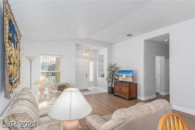 living room featuring a chandelier, vaulted ceiling, and light hardwood / wood-style flooring