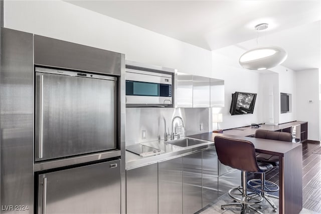 kitchen featuring a kitchen breakfast bar, sink, light wood-type flooring, black electric cooktop, and stainless steel counters