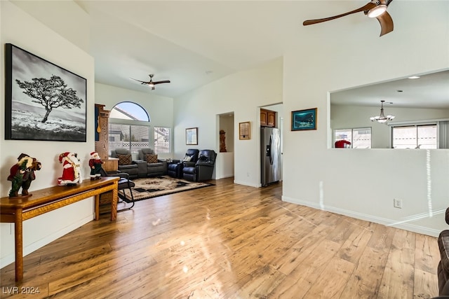 living room featuring ceiling fan with notable chandelier, light wood-type flooring, and vaulted ceiling