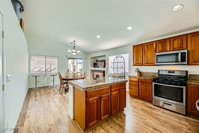 kitchen featuring appliances with stainless steel finishes, decorative light fixtures, light hardwood / wood-style flooring, a kitchen island, and lofted ceiling