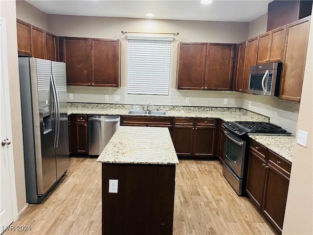 kitchen featuring light stone countertops, appliances with stainless steel finishes, sink, light hardwood / wood-style floors, and a kitchen island