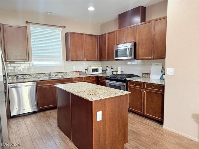 kitchen with decorative backsplash, light stone counters, stainless steel appliances, a center island, and light hardwood / wood-style floors