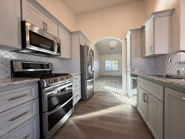 kitchen with dark wood-type flooring, sink, appliances with stainless steel finishes, tasteful backsplash, and light stone counters