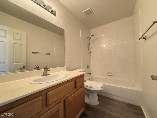 full bathroom featuring vanity, a textured ceiling, tiled shower / bath combo, hardwood / wood-style flooring, and toilet