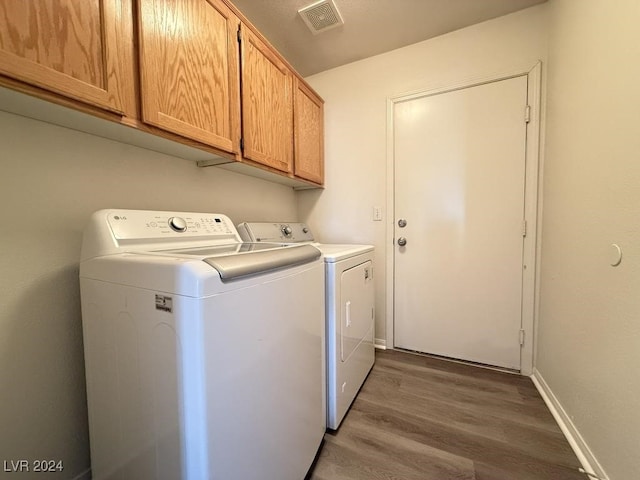 laundry area featuring washing machine and clothes dryer, dark hardwood / wood-style flooring, and cabinets