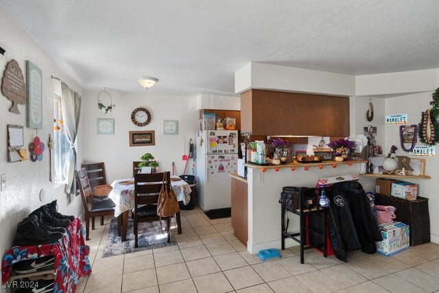 4740 Corsaire Ave, Las Vegas, NV 89115 - kitchen featuring freestanding refrigerator, light tile patterned floors, a peninsula, and brown cabinetry