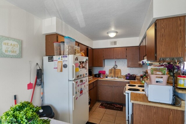 4740 Corsaire Ave, Las Vegas, NV 89115 - kitchen featuring white appliances, a sink, light countertops, light tile patterned floors, and brown cabinets